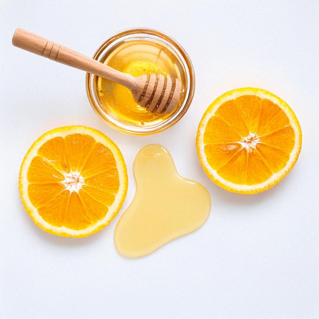 Jar of honey with a wooden dipper and sliced oranges on a white background